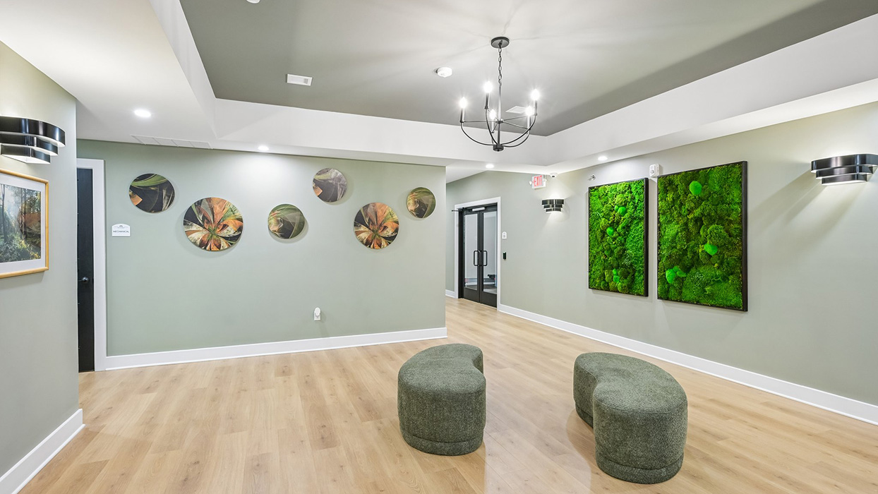 Community lounge hallway with decorative wall art, modern lighting, and soft seating along wood-style flooring