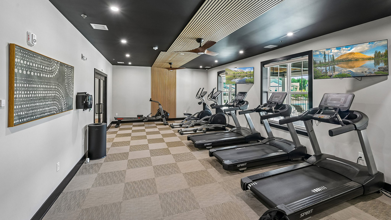 Fitness center with treadmills, cardio machines, and wall-mounted TVs overlooking large windows