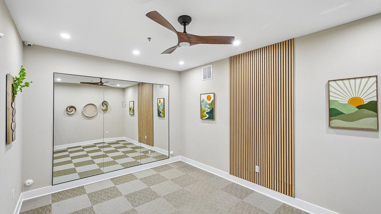 Yoga or flex studio with mirrored wall, ceiling fan, and open space for exercise or stretching