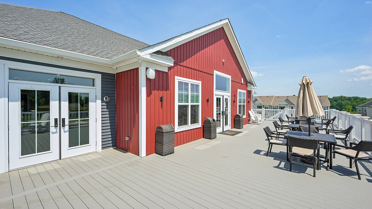 Outdoor clubhouse deck with patio seating, umbrellas, and red-paneled exterior overlooking neighborhood homes