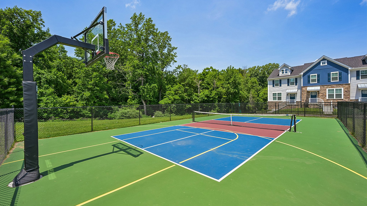 Pickleball and basketball court with fenced perimeter and surrounding greenery near residential buildings