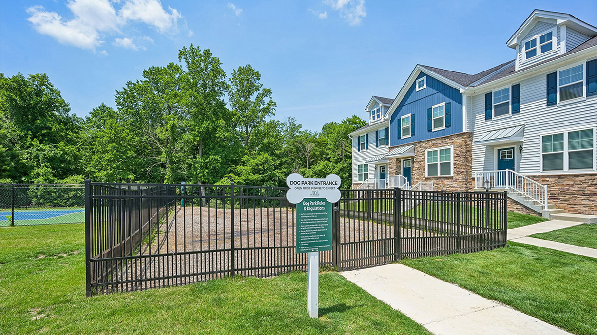 Dog park with fenced enclosure, posted rules sign, and nearby townhomes in the background