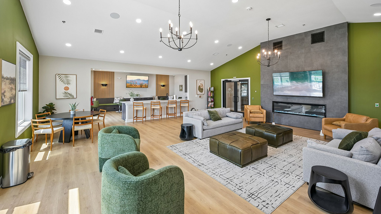 Resident lounge with open-concept seating, modern fireplace feature wall, and kitchen bar with high-top chairs