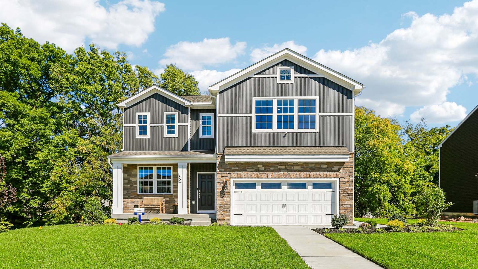 Exterior front view of a two-story Galen home featuring covered porch, ironstone board and batten siding, stone accents, and stone siding surrounding a white two car garage in Bennington.