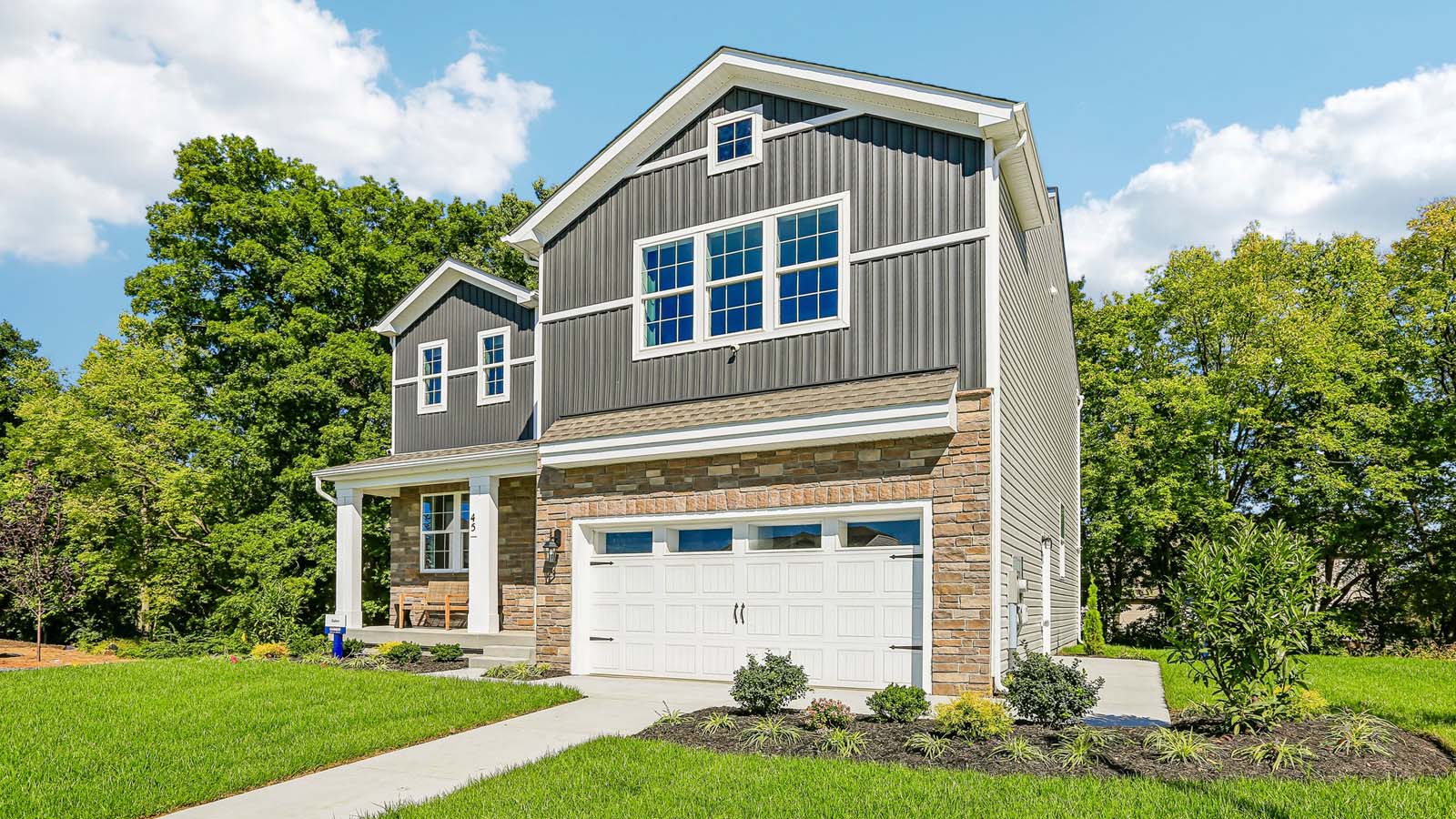Exterior front view of a two-story Galen home featuring covered porch, ironstone board and batten siding, stone accents, and stone siding surrounding a white two car garage in Bennington.
