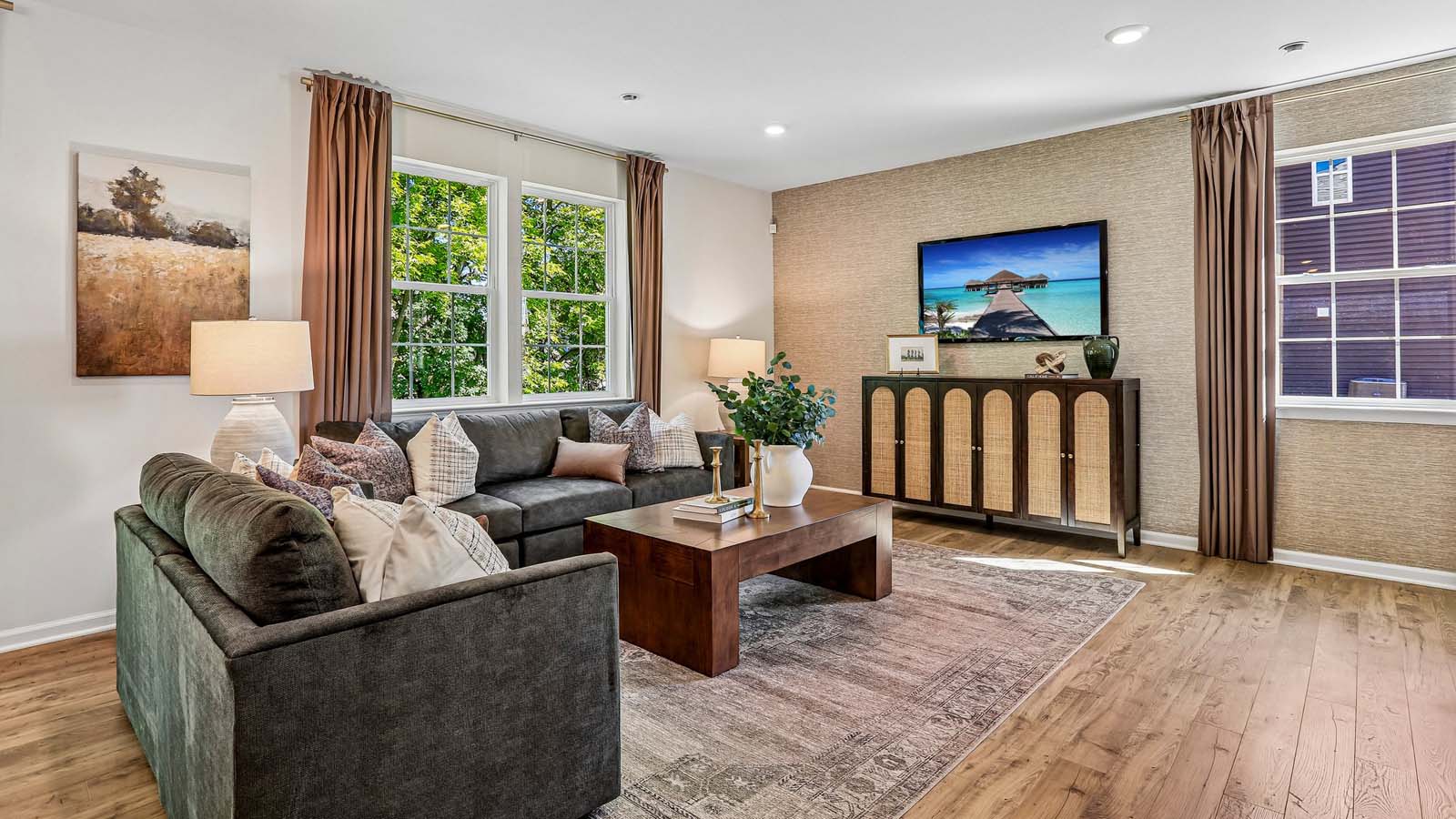 Open-concept living area with three large windows and L-shaped sectional perfect for conversation and entertainment.