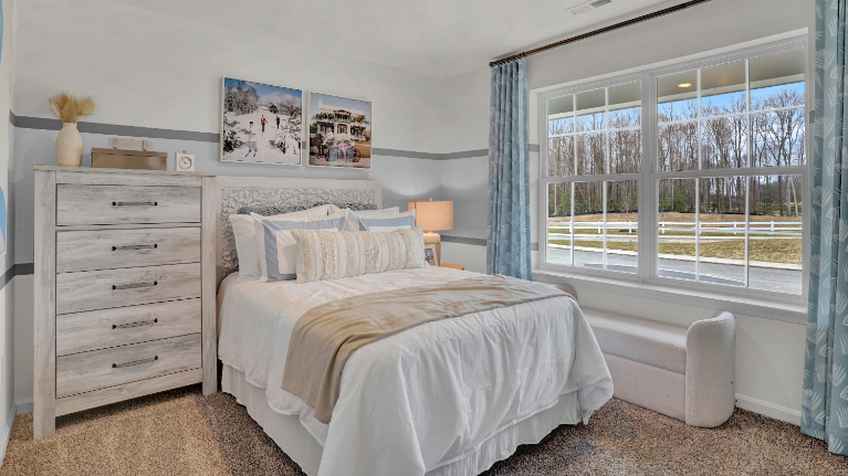 Bedroom in a new home with large window, plush carpeting, and soft neutral bedding filled with natural light