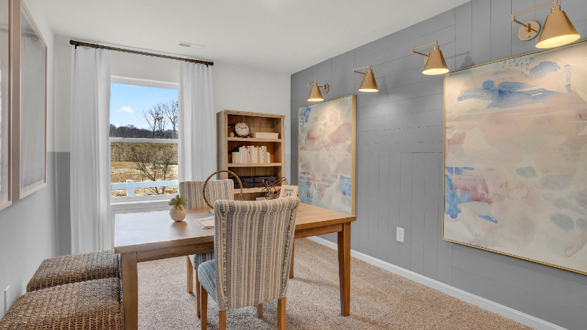 Dining room or flex space with wood table, accent wall art, and natural light creating a warm setting in this new home