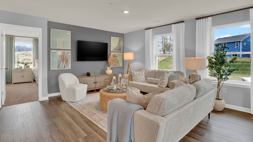 Open-concept living room with large windows, cozy seating, and abundant natural light in this inviting new home