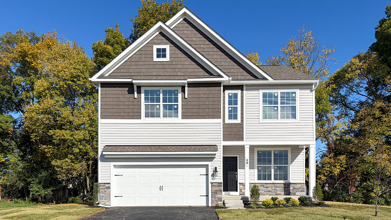 A photo of the front of a two-story Penwell home with sterling siding and ironstone shake accent siding, dakota ledgestone knee wall, white accents, and a tricorn black front door.
