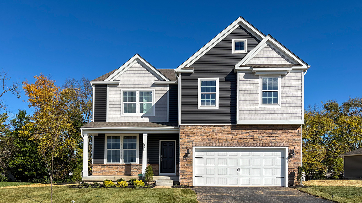 A photo of a two-story Henson home with misty blue and gray siding, stone kneewall, brown front door, and stone siding surrounding a white two car garage.
