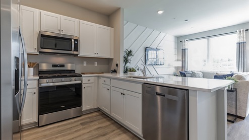 U shaped kitchen with stainless steel appliances and white counter tops and cabinetry.