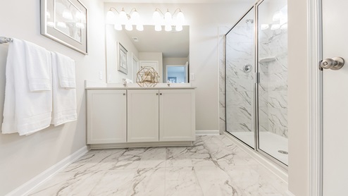 Connecting bathroom to the bedroom with two double windows. White and gray marble tile flooring and shower. Single white sink vanity.