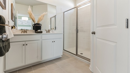 Connecting bath to the primary bedroom with double sink white vanity and glass door shower.