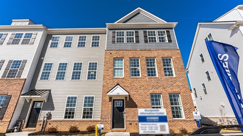 Exterior front image of three story townhome with two car white garage in the back.