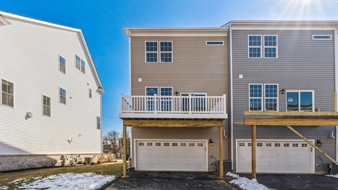Exterior back image of three story townhome with two car white garage and back deck.
