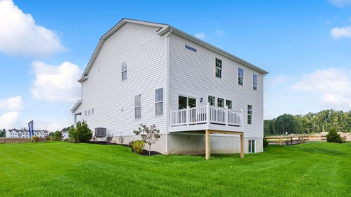 Exterior back image of the three story white horizontal paneling house with raised back porch and door to exit the basement.