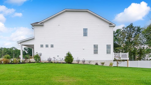 Exterior side image of the three story white horizontal paneling house with front porch and raised back porch.