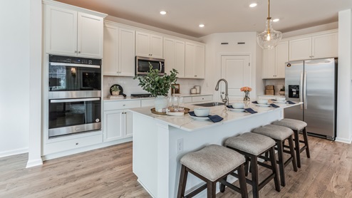 Gourmet kitchen with large island with white counter tops and white cabinetry with stainless steel appliances.