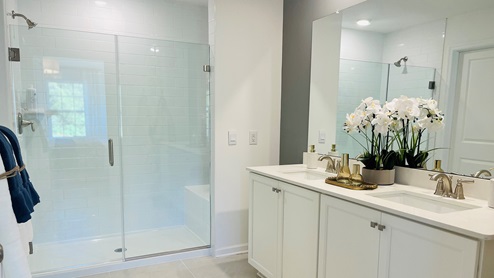 Primary bathroom with double sink white counter top and white vanity and glass door shower.