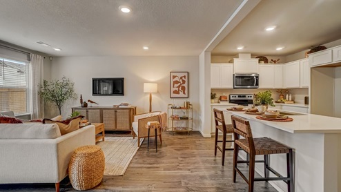 open-concept living room, ining area and kitchen with a pantry, island, stainless steel appliances, quartz countertops, eat bar, and white shaker-style cabinets