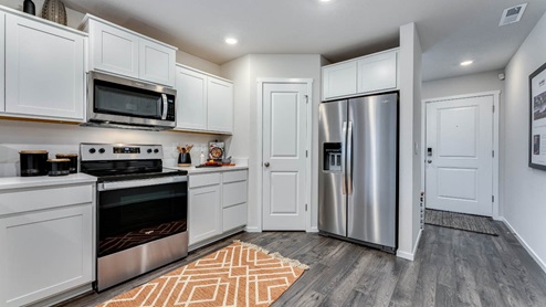 u-shaped kitchen with stainless steel appliances, quartz countertops, and a full size pantry