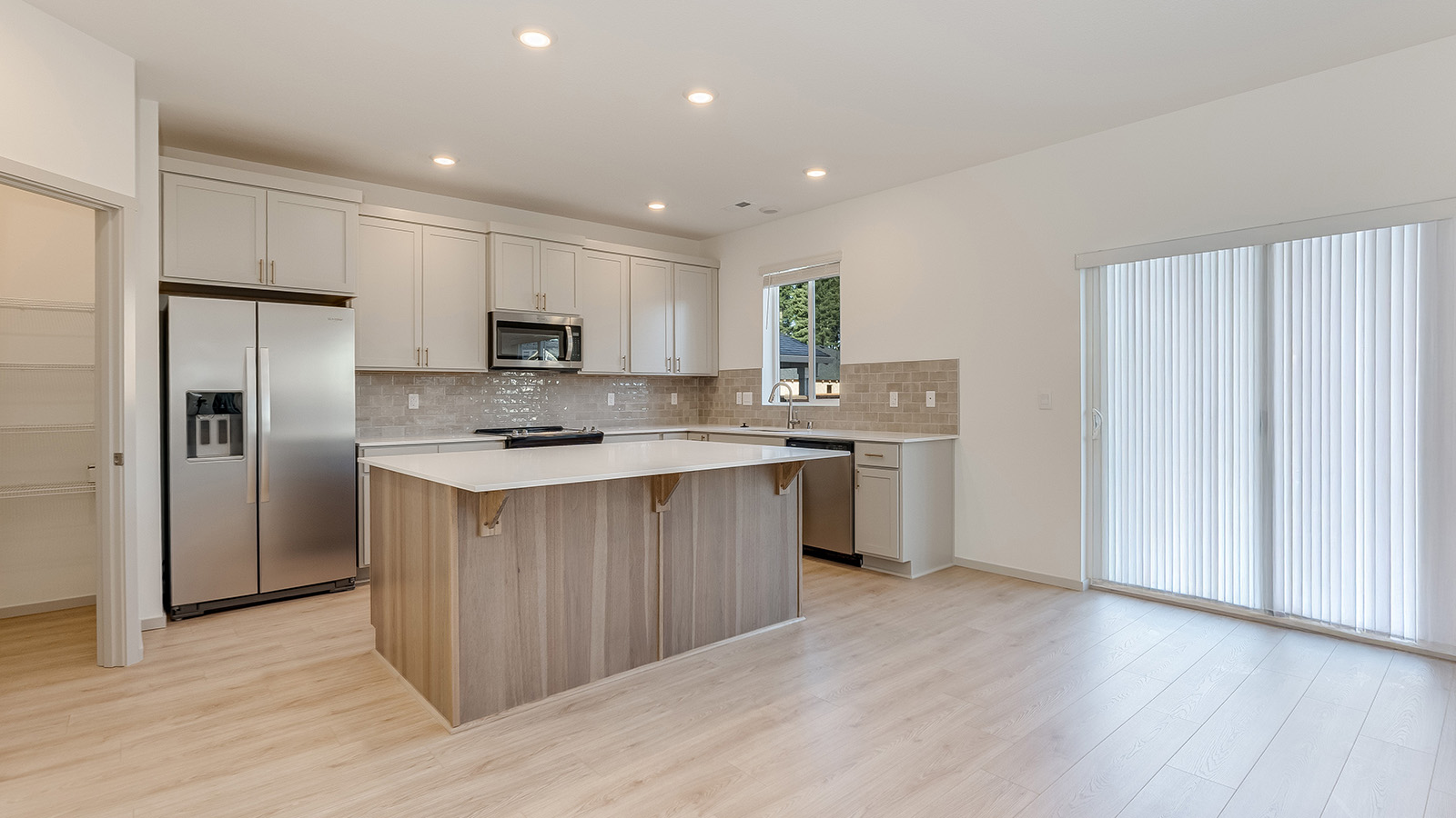 Kitchen with shaker cabinets, quartz counters, stainless steel appliances, pantry, and an island with a breakfast bar