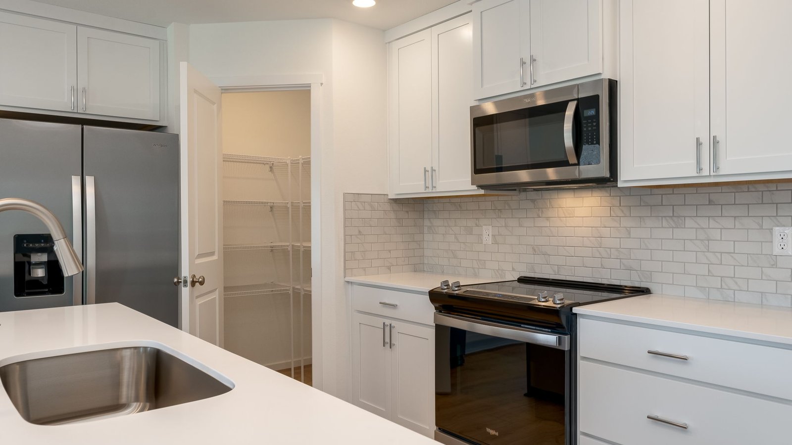 Kitchen with shaker cabinets, quartz counters, stainless steel appliances, pantry, and an island with a breakfast bar