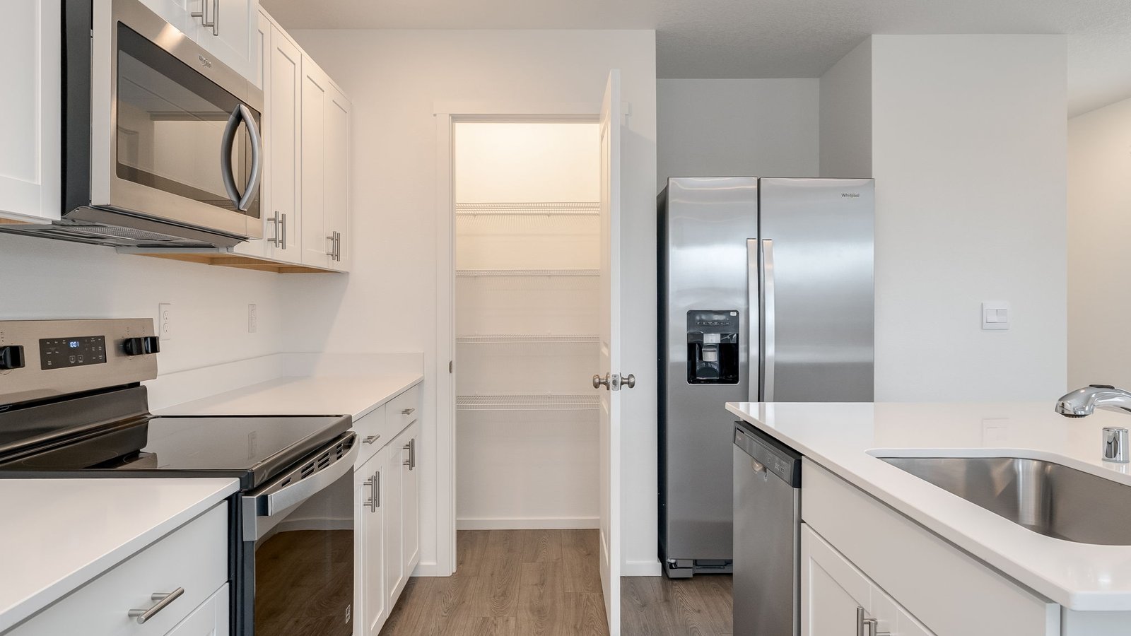 Kitchen with shaker cabinets, quartz counters, stainless steel appliances, pantry, and an island with a breakfast bar