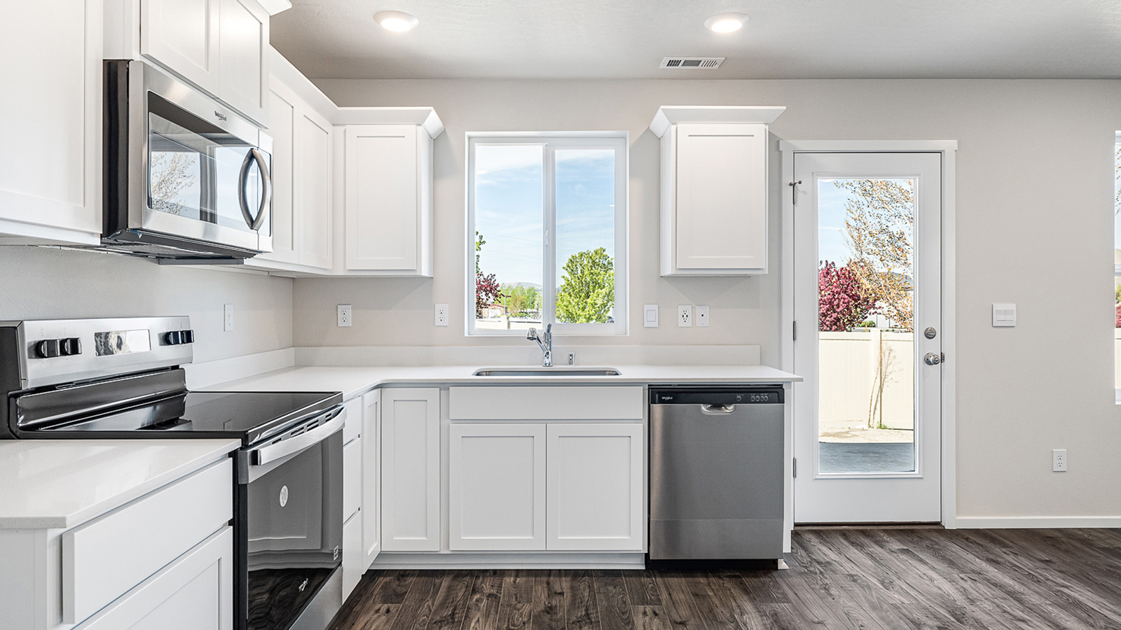 L-shaped kitchen with shaker cabinets, quartz counters, stainless steel appliances, and a pantry