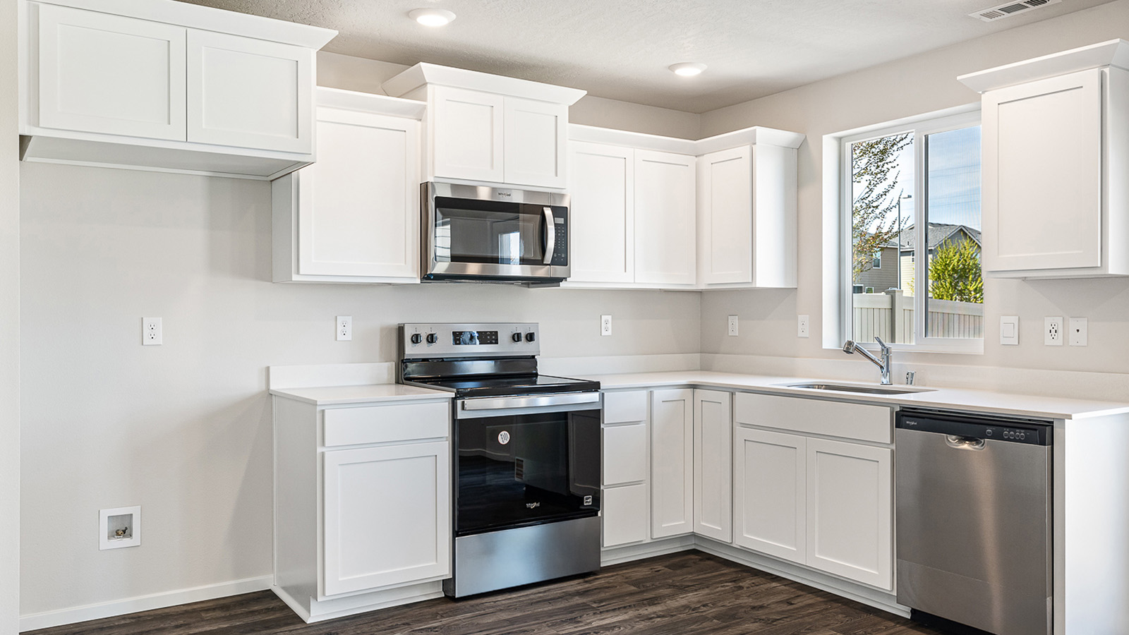 L-shaped kitchen with shaker cabinets, quartz counters, stainless steel appliances, and a pantry