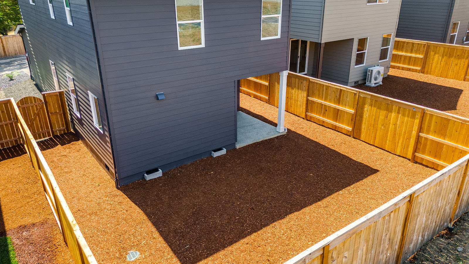 fully fenced backyard with bark chips and a patio