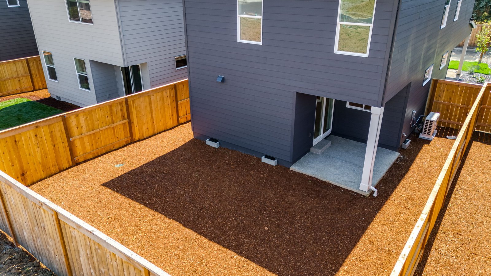 fully fenced backyard with bark chips and a patio