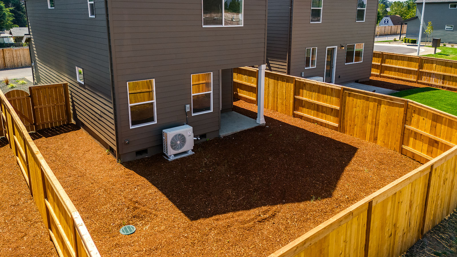 fully fenced backyard with bark chips and a patio