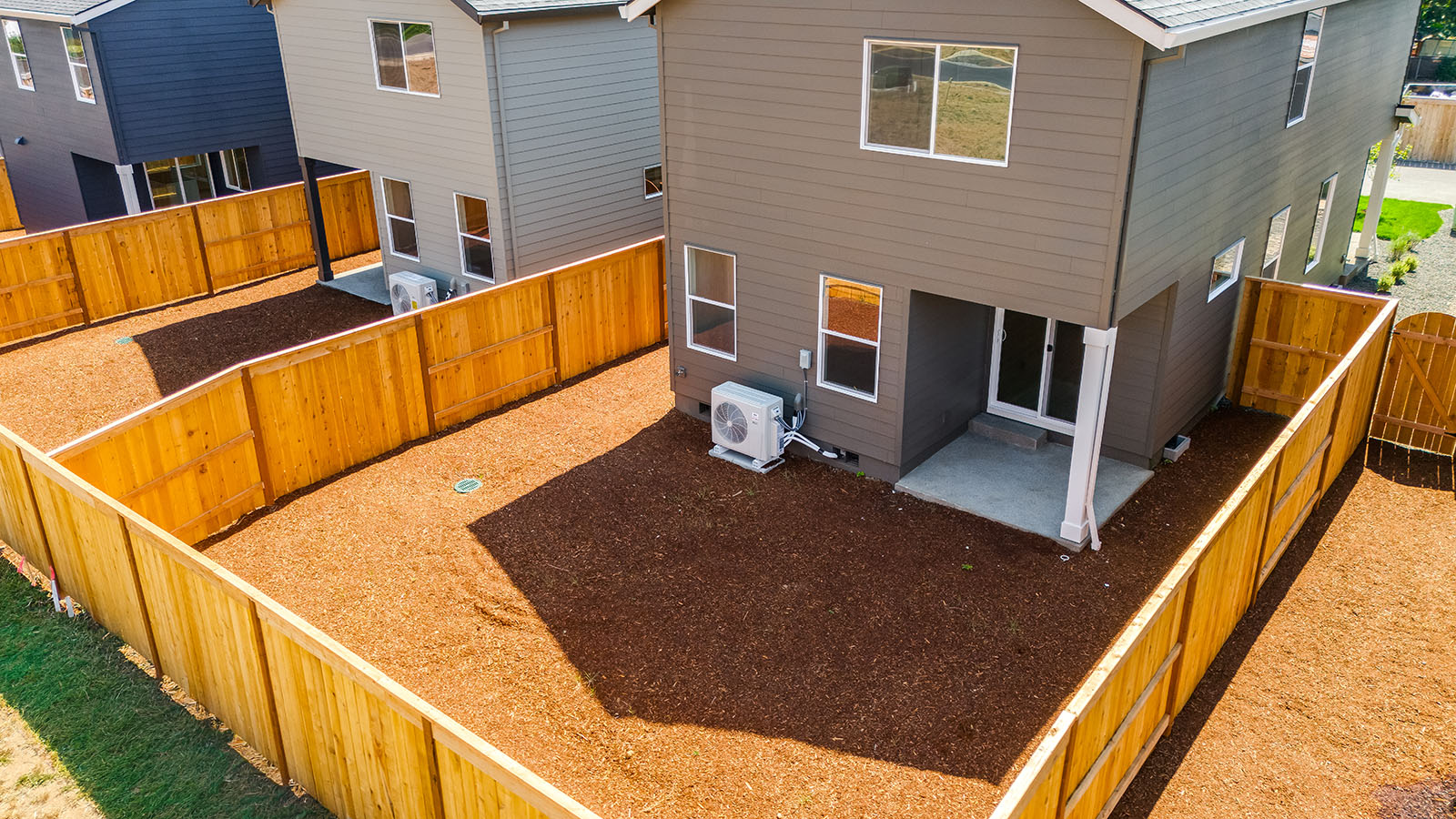 fully fenced backyard with bark chips and a patio