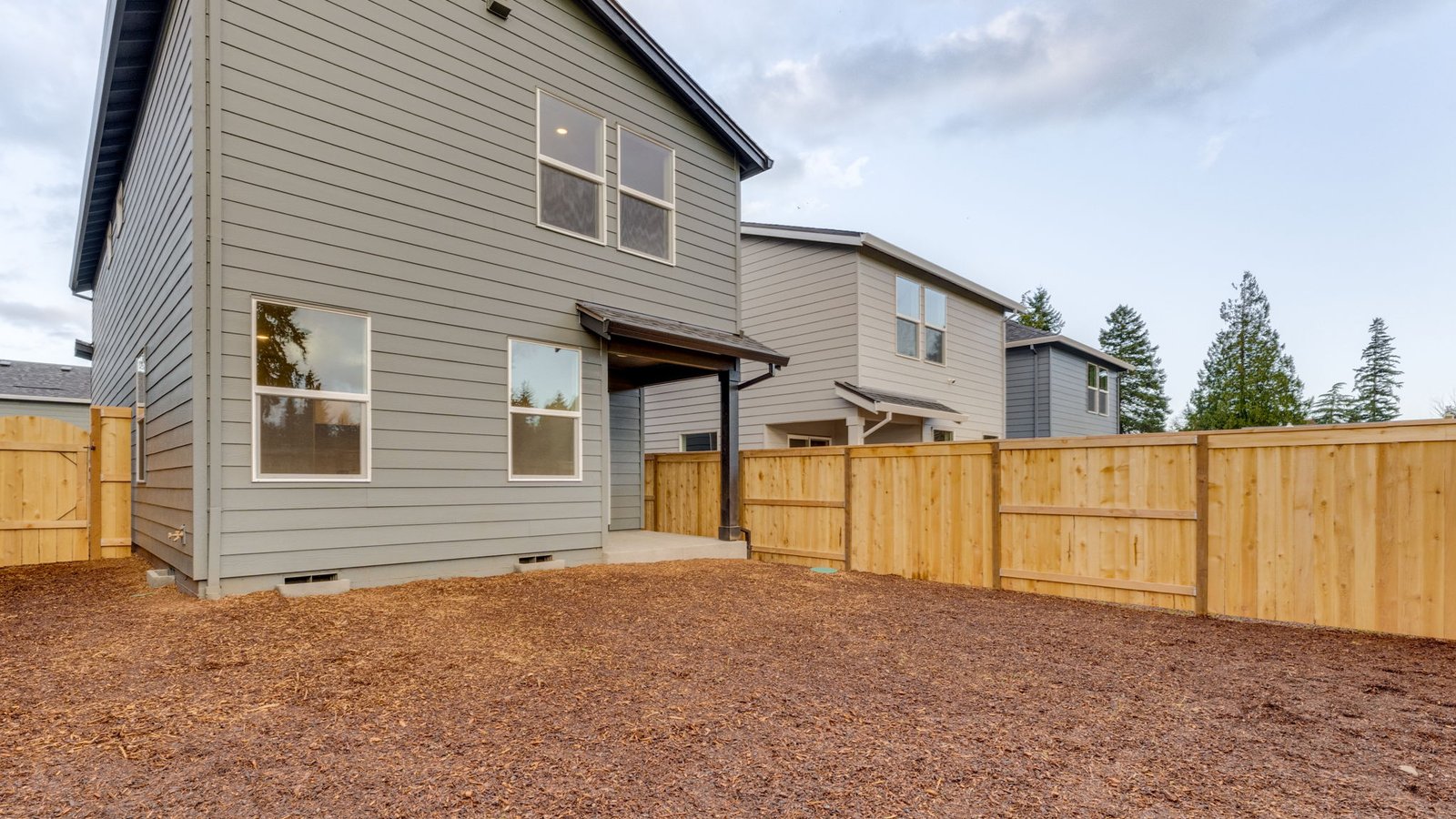 fully fenced backyard with bark chips and a patio