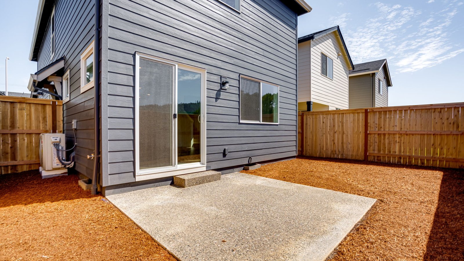 fully fenced backyard with bark chips and a patio