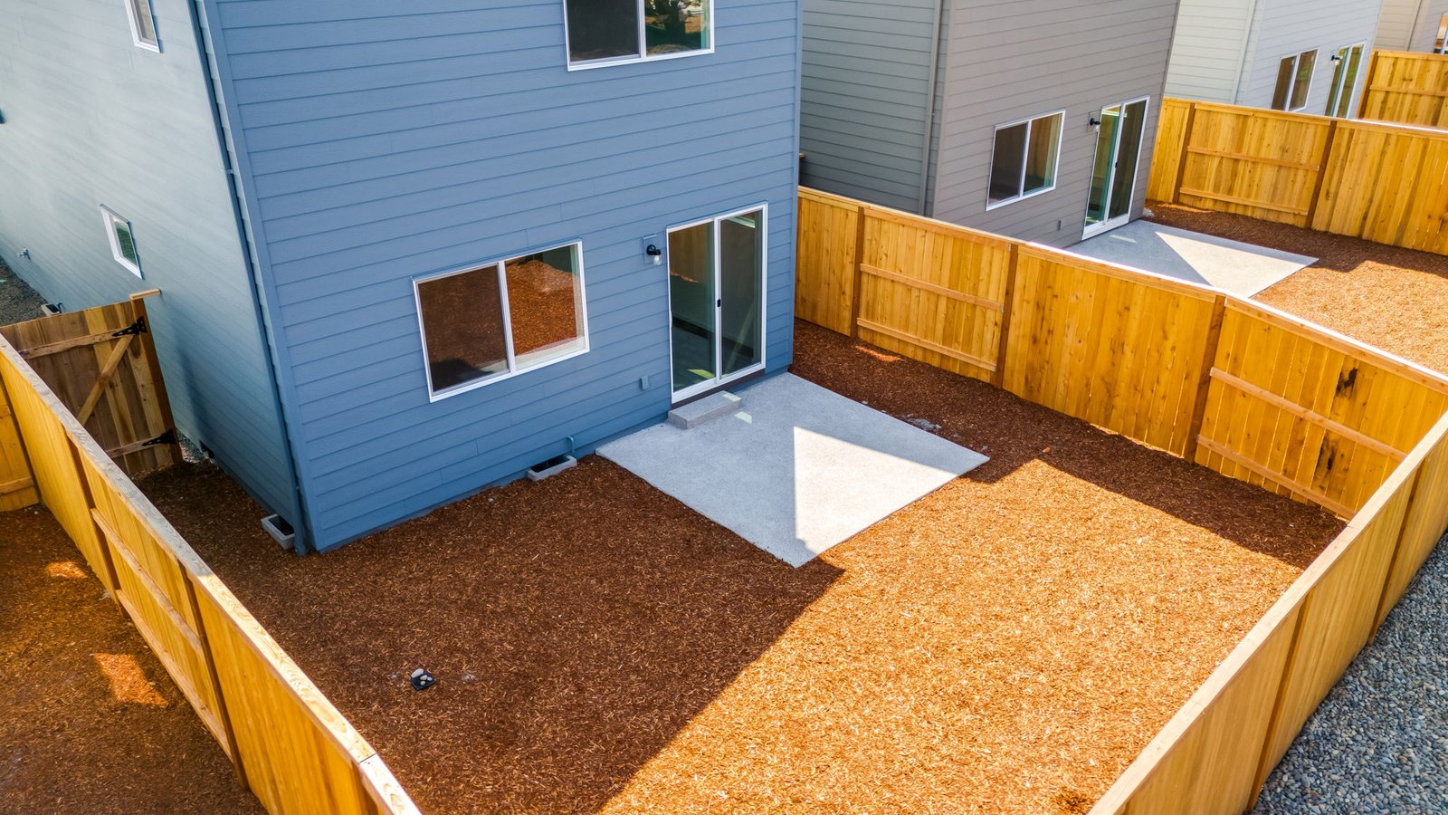 fully fenced backyard with bark chips and a patio