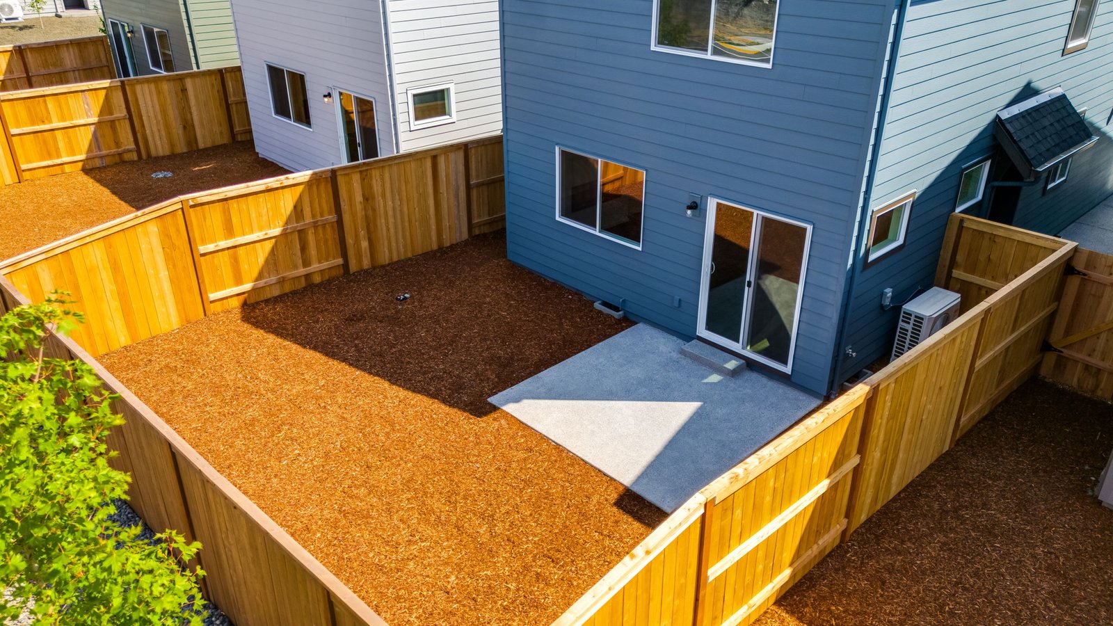 fully fenced backyard with bark chips and a patio