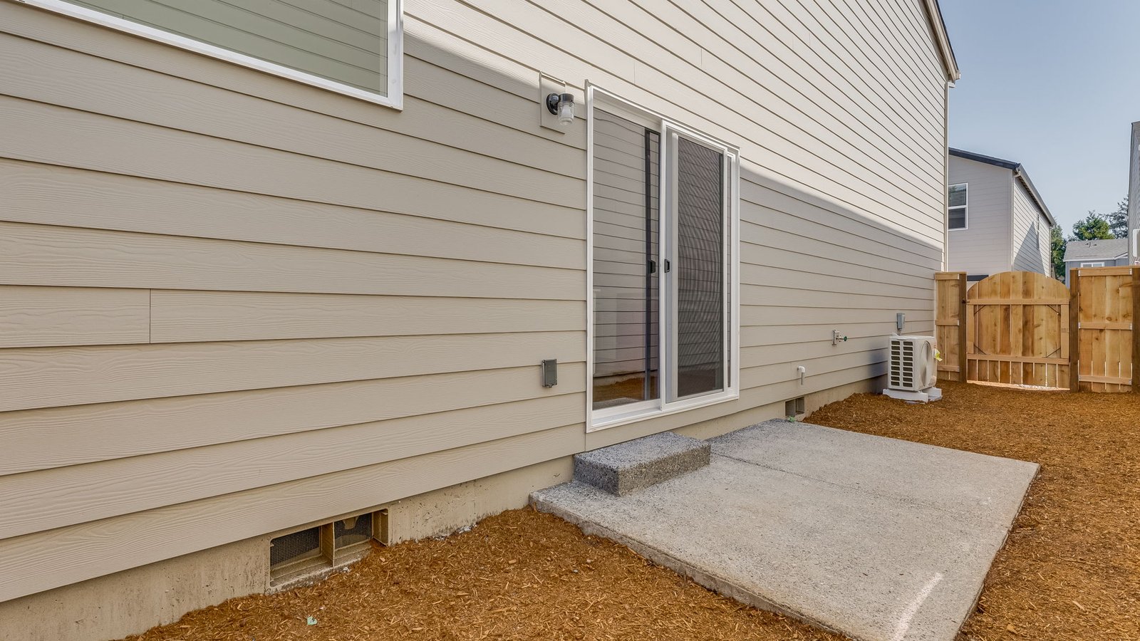 fully fenced sideyard with bark chips and a patio
