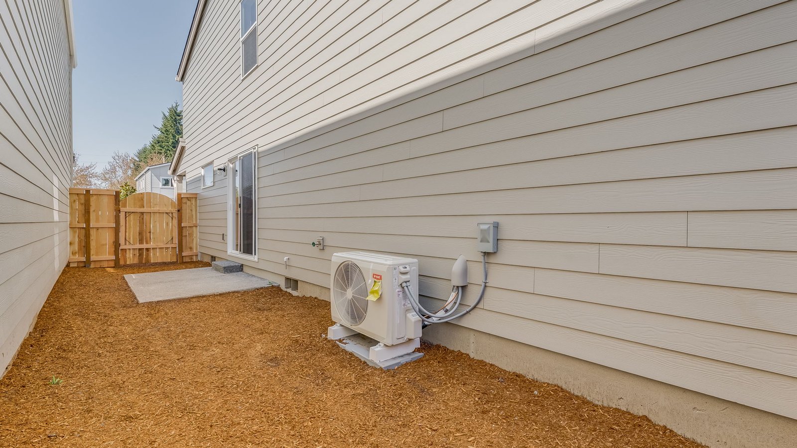 fully fenced sideyard with bark chips and a patio