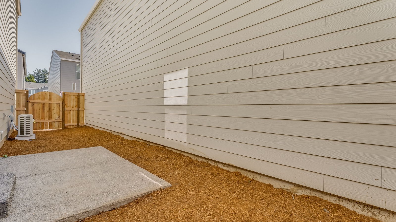 fully fenced sideyard with bark chips and a patio