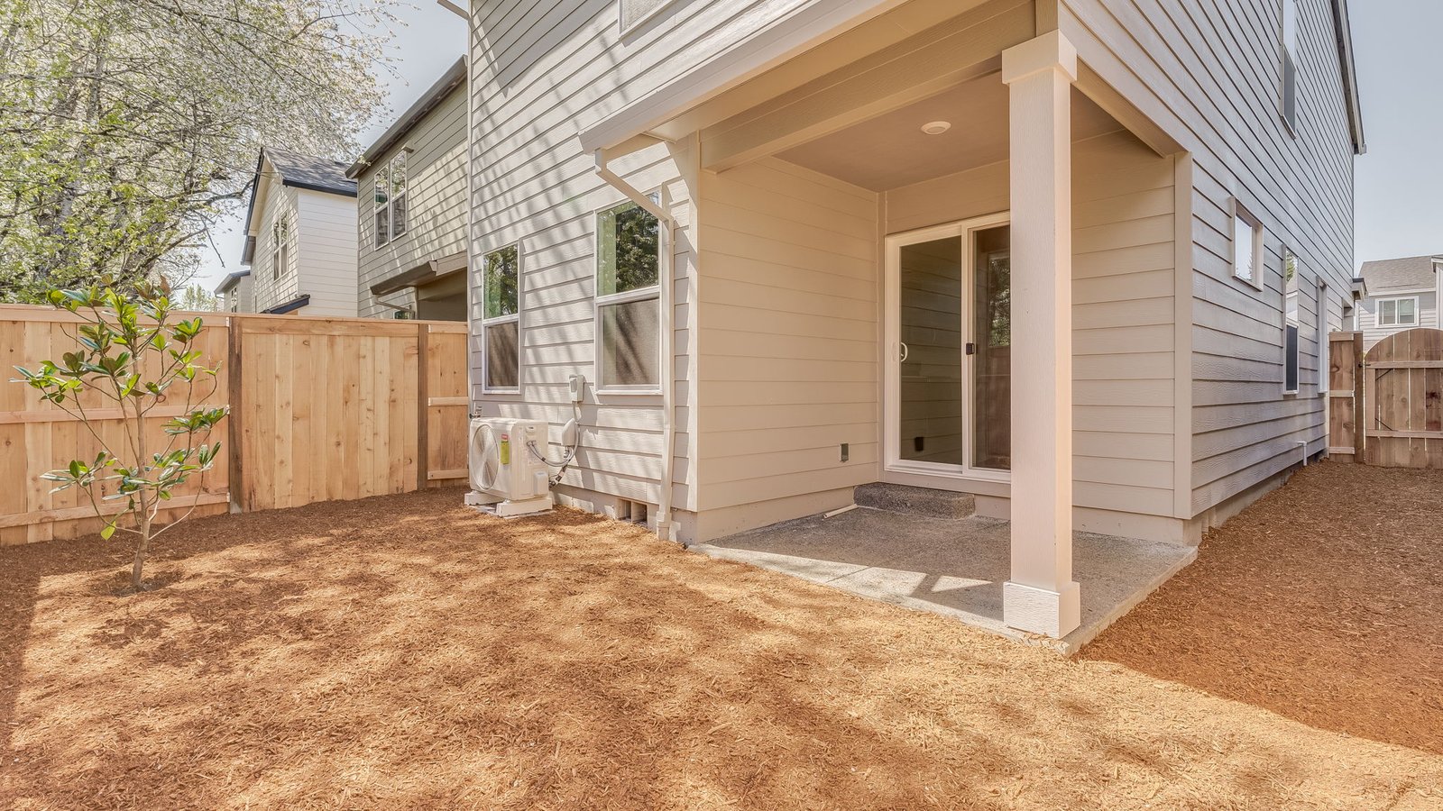 fully fenced backyard with bark chips and a patio