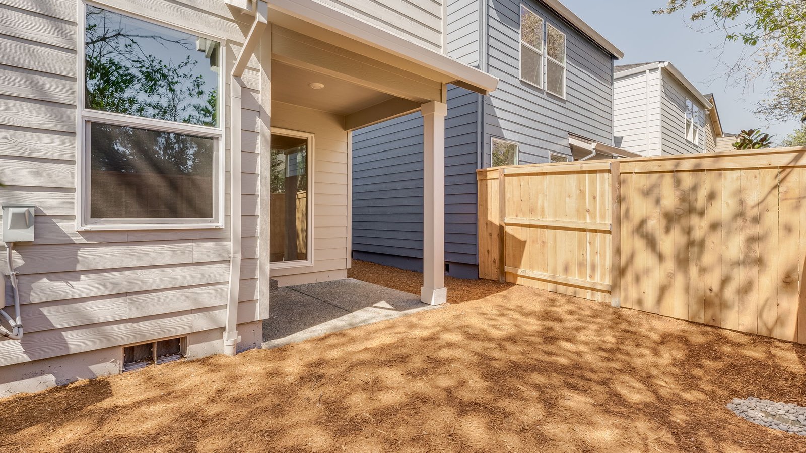 fully fenced backyard with bark chips and a patio
