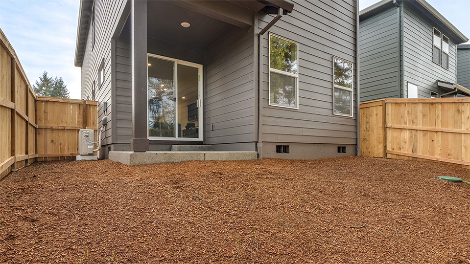 fully fenced backyard with bark chips and a patio
