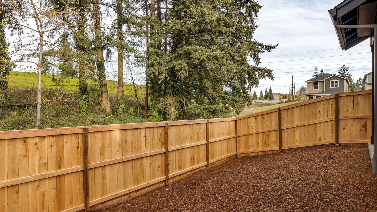 fully fenced backyard with bark chips and a patio