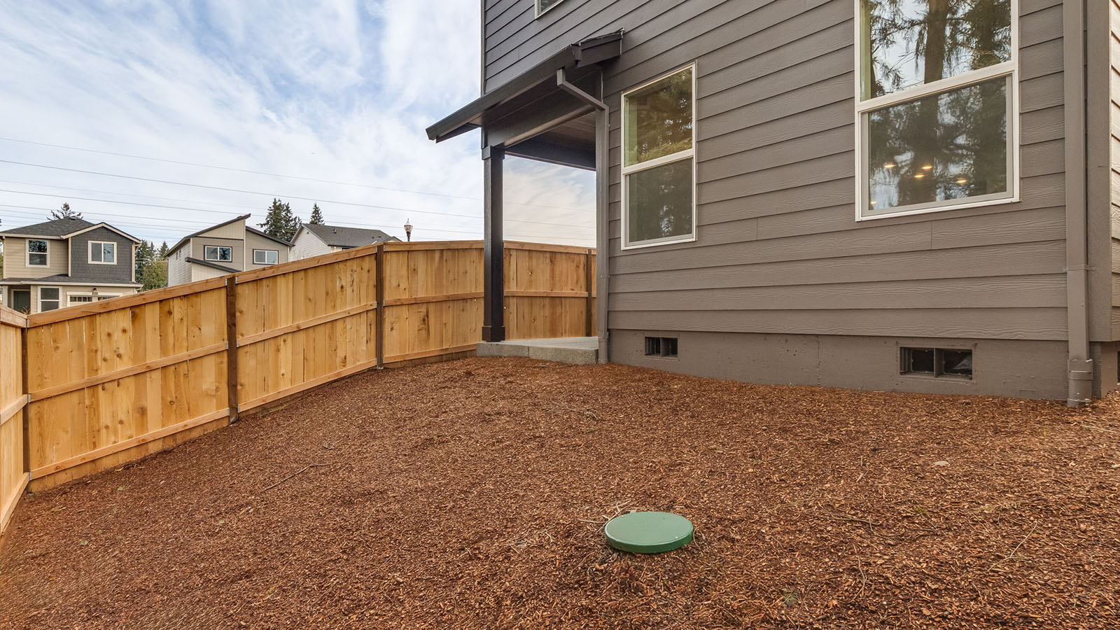fully fenced backyard with bark chips and a patio