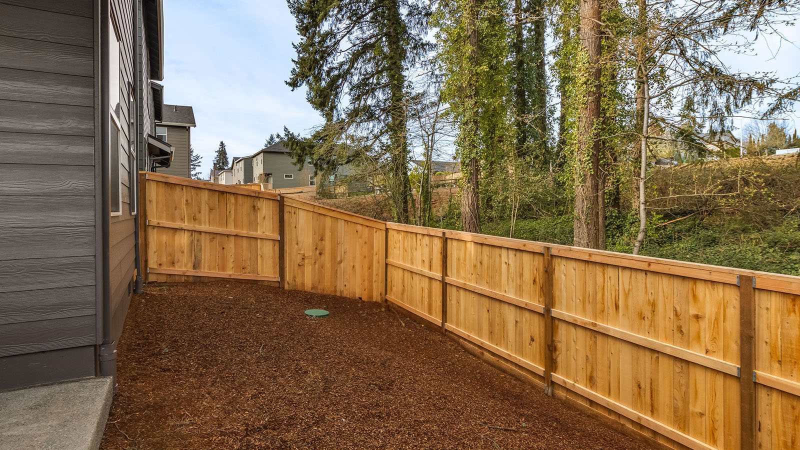 fully fenced backyard with bark chips and a patio