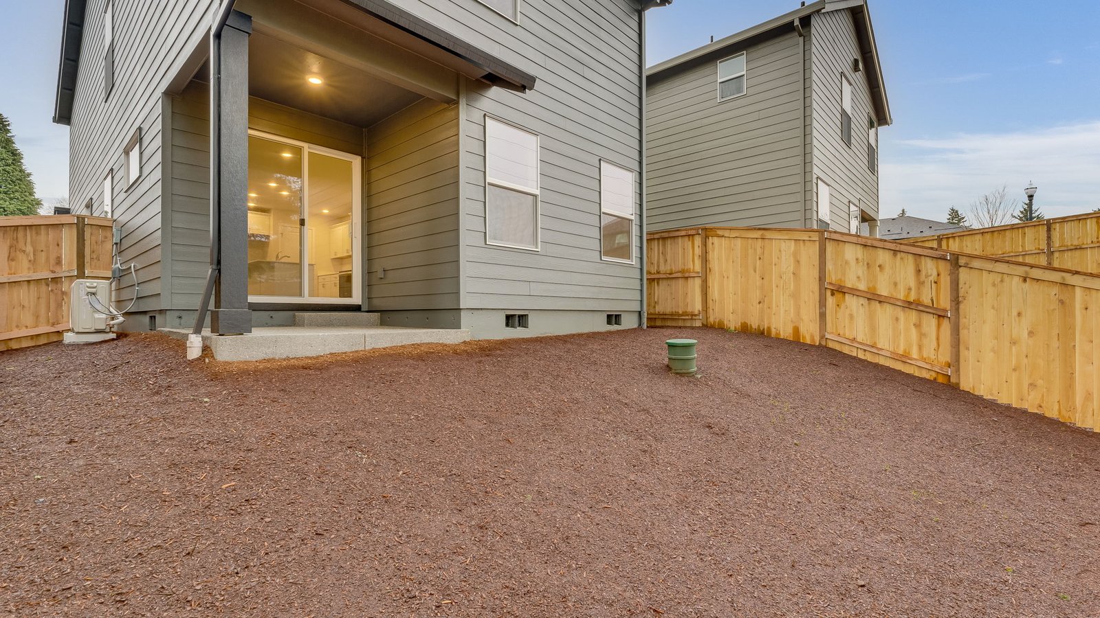fully fenced backyard with bark chips and a patio