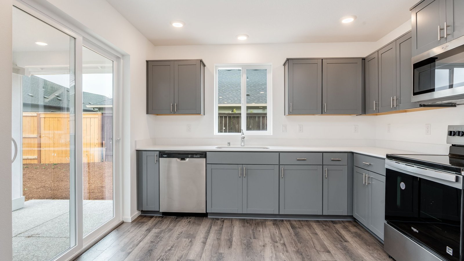 L-shaped kitchen with shaker cabinets, quartz counters, stainless steel appliances, and a pantry